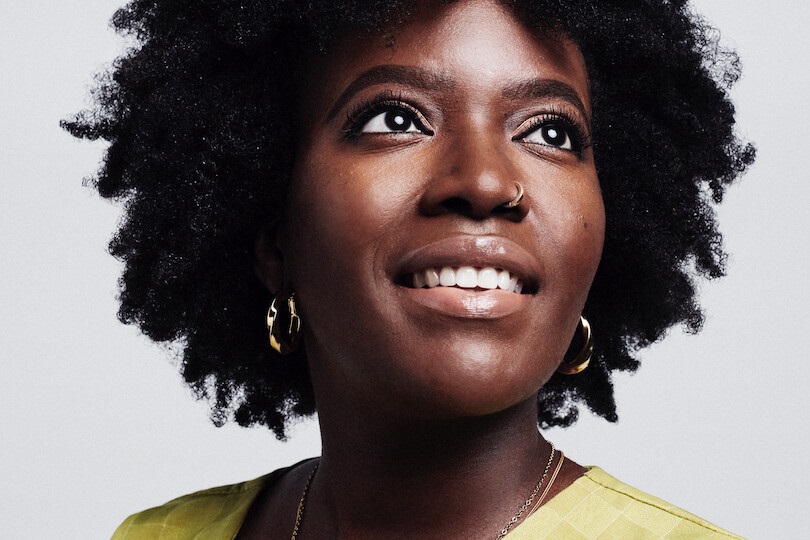 Headshot of a woman looking upwards to her left whilst smiling.