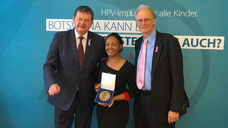 Two men and a woman, standing in front of a backdrop, shows an award.
