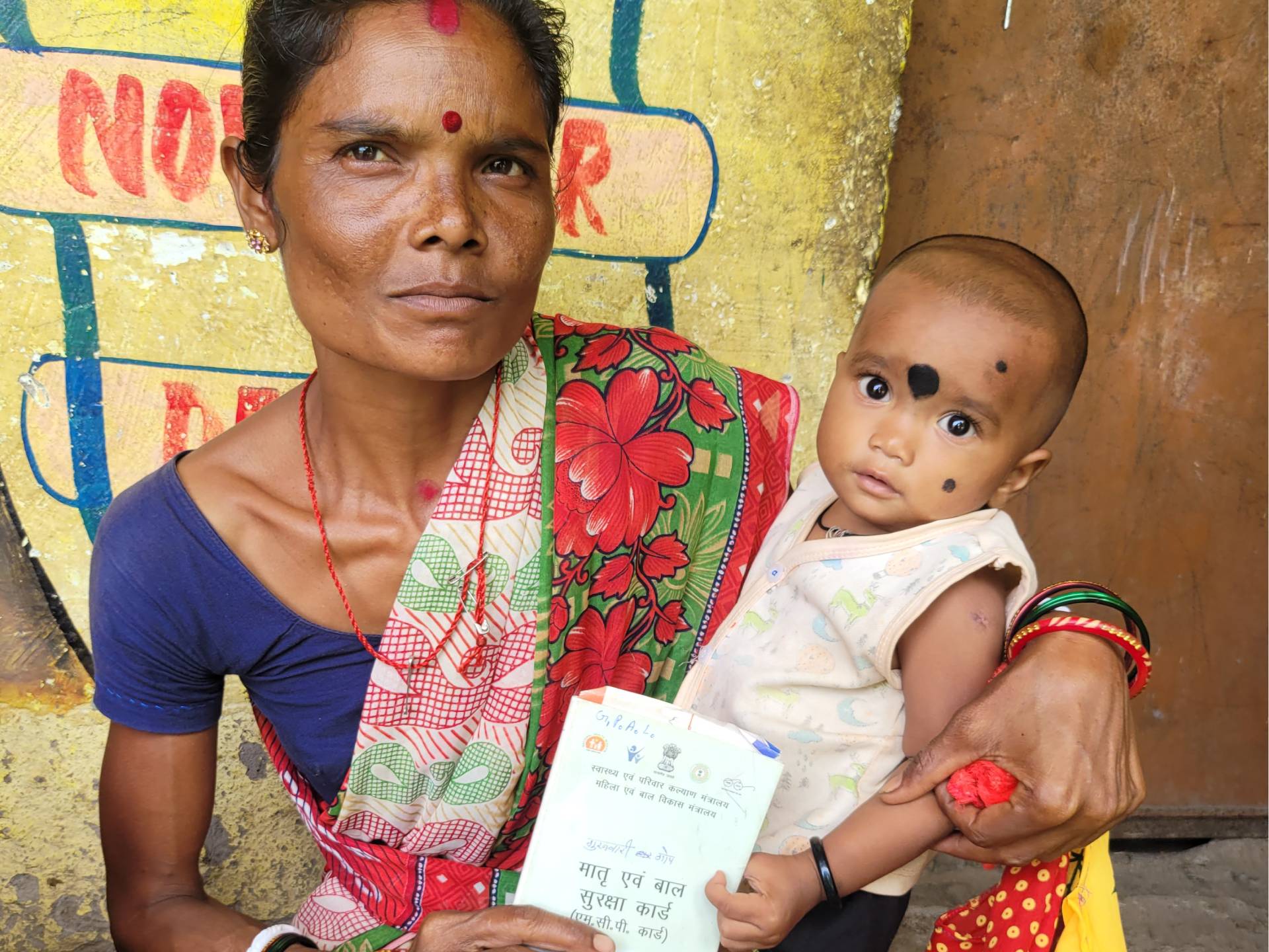 A mother and child with their Mother and Child Protection card at a monthly Village Health Nutrition Day session in Tonto block
