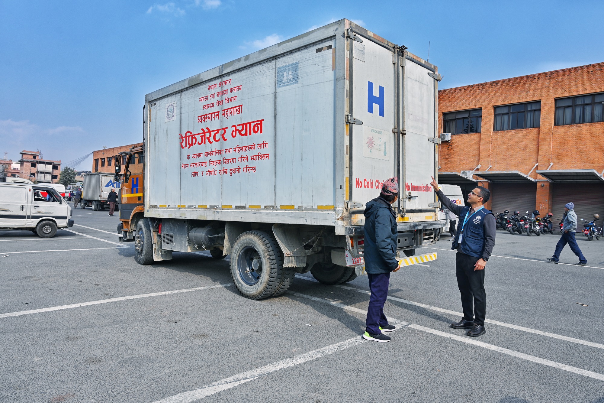 A WHO personnel is outside a vaccine truck equipped with cold chain technology, discussing the first batch of essential cancer medicines under the Global Platform for Access to Childhood Cancer Medicines