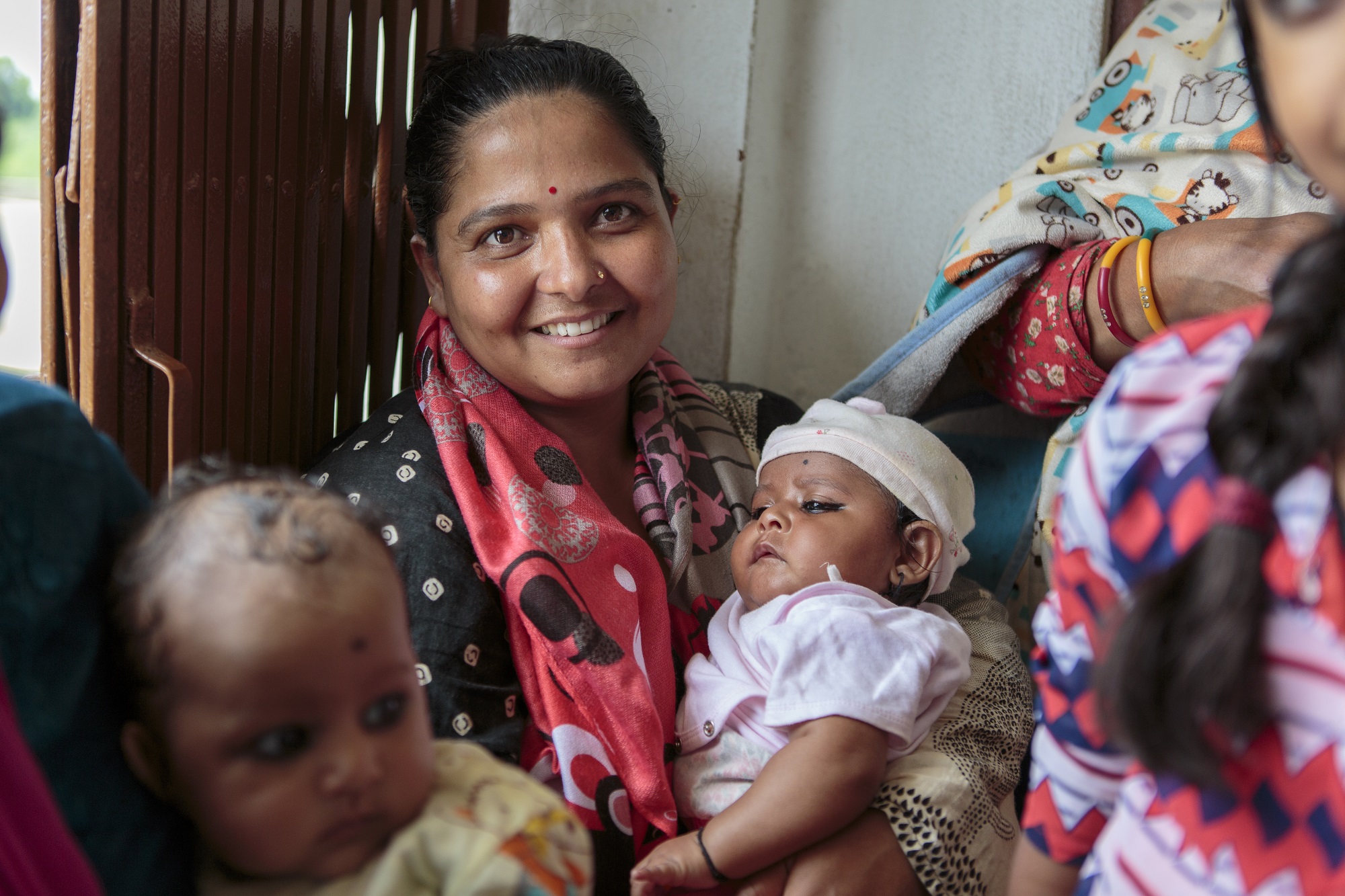 A woman holding her baby sits in line with other mothers and babies, waiting for routine immunization in Bagmati Province, Nepal