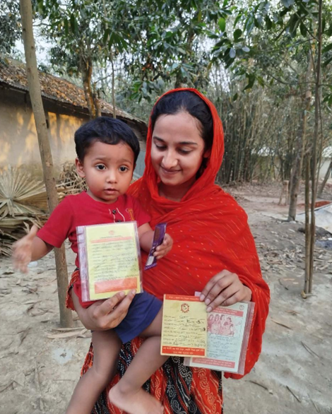 Mother in a red shawl holding her young son as both display their immunization cards