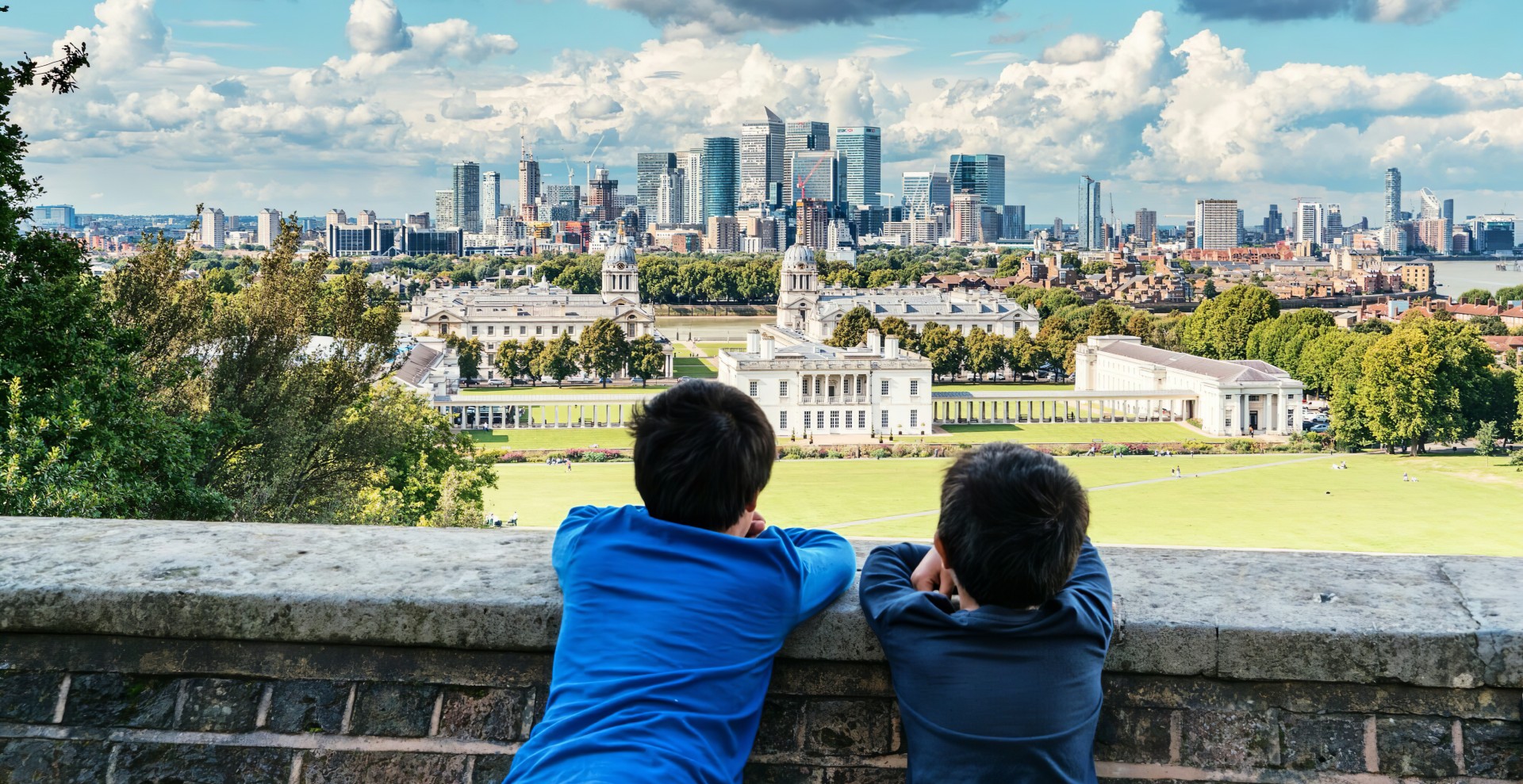 Green city, London, United Kingdom Two boys leaning against a wall, gazing at a city and its lush green surroundings.