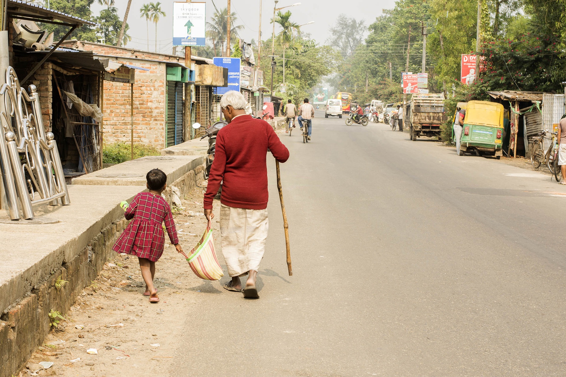 A little girl helps an old man carry a bag down a street