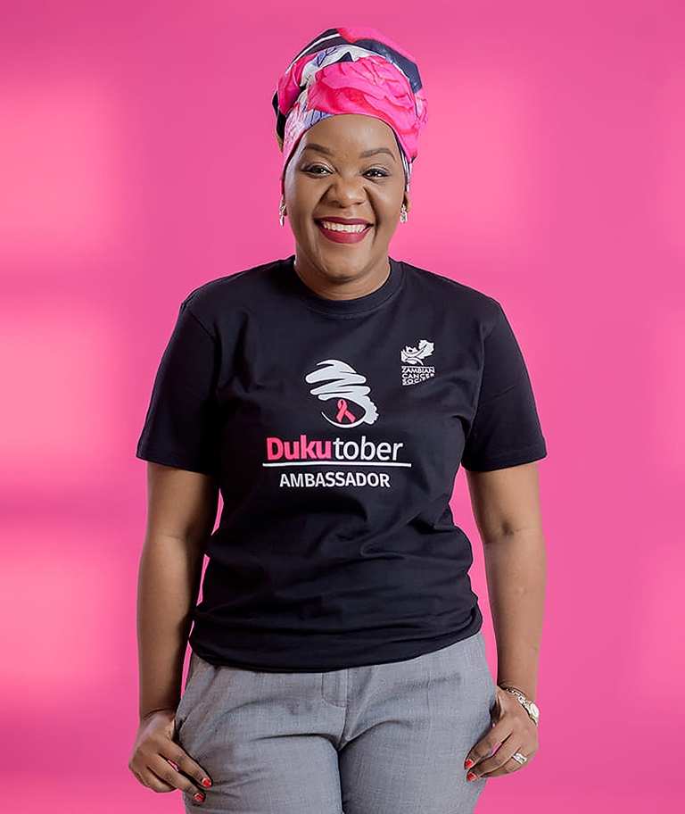 A magenta social media tile with a photo of a woman wearing a Zambian Cancer Society t-shirt.