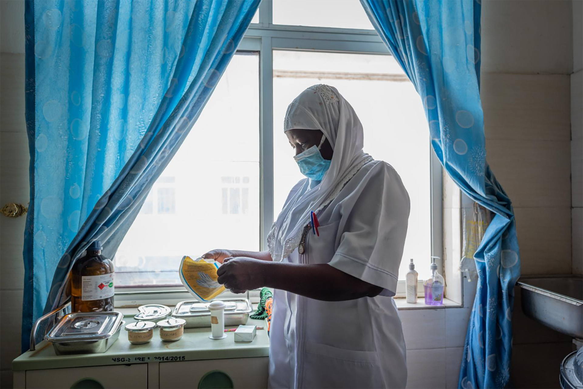 A health care worker in a clinic wearing a mask opening a packet of disposable gloves,