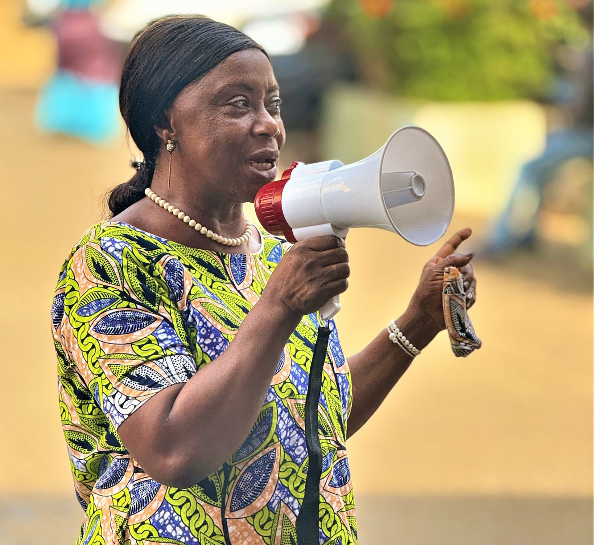 A female health worker is calling through a hand held loud speaker.