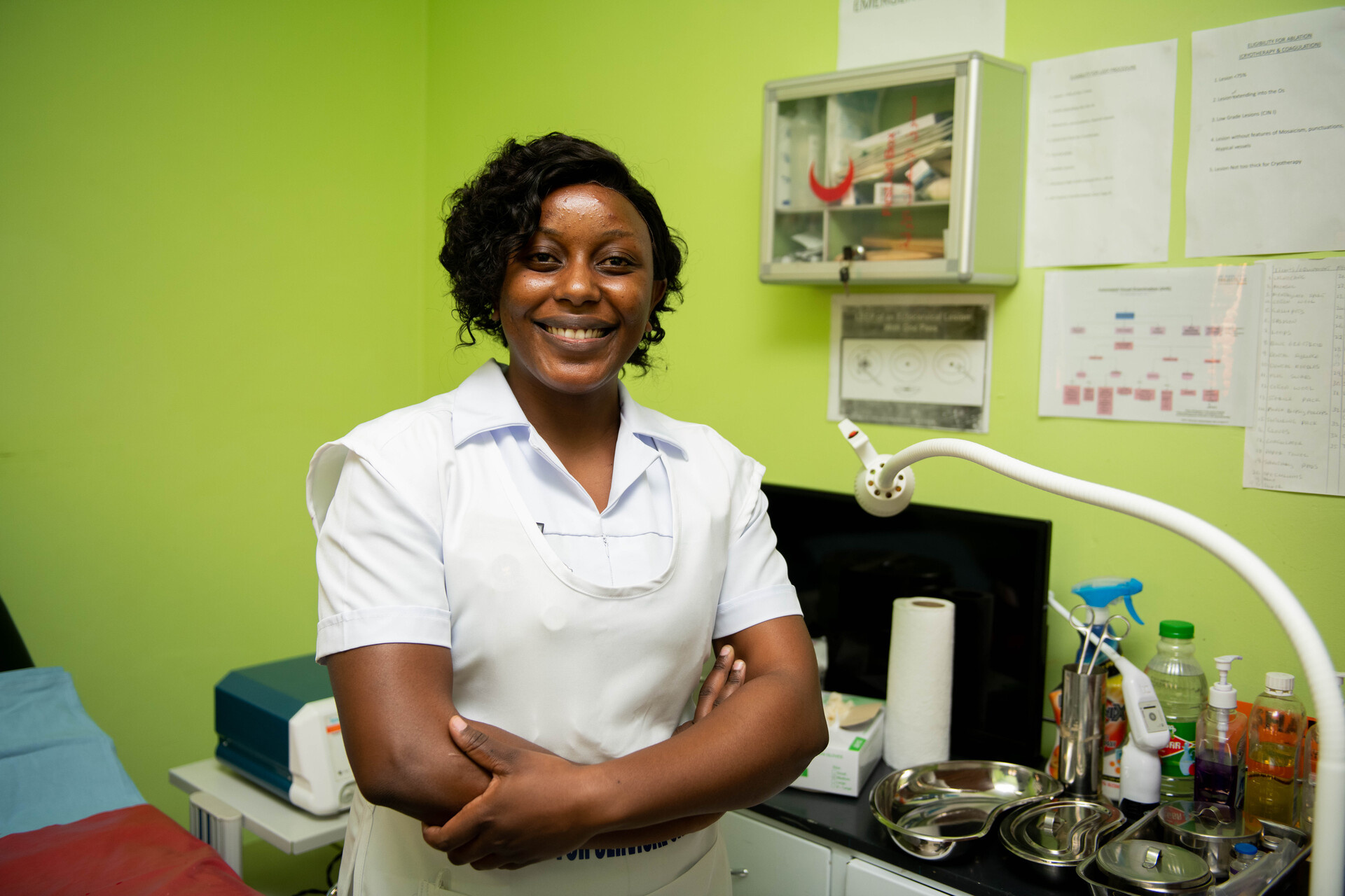 A nurse is standing and smiling in a treatment room.