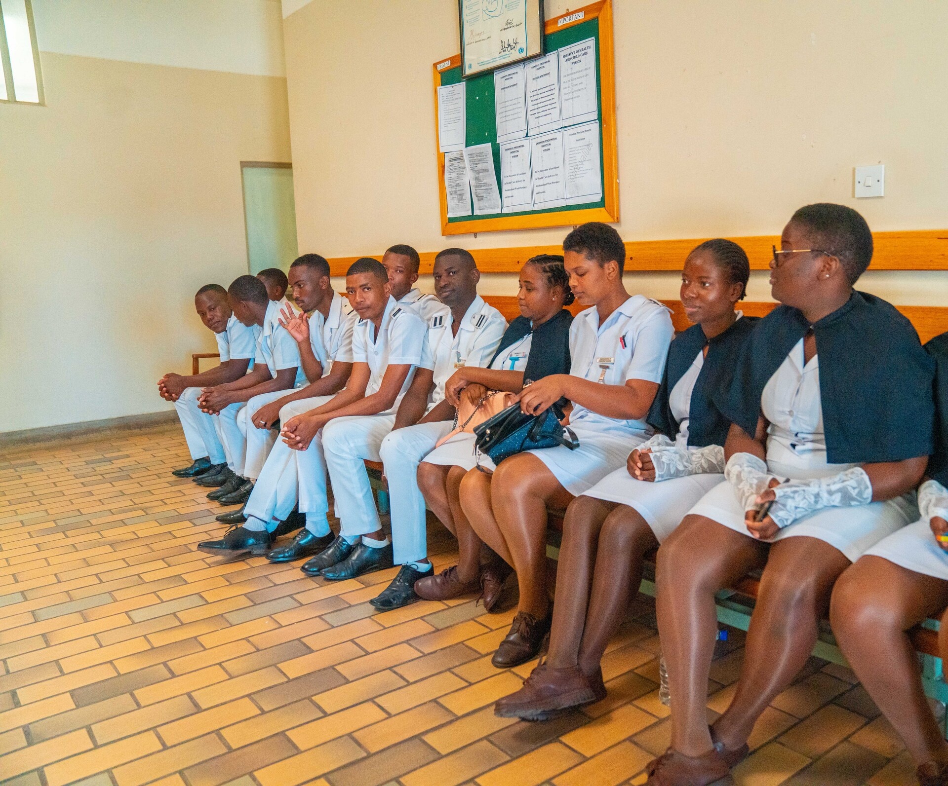 A mixed group of trainee doctors and nurses sitting in a row at a clinic.