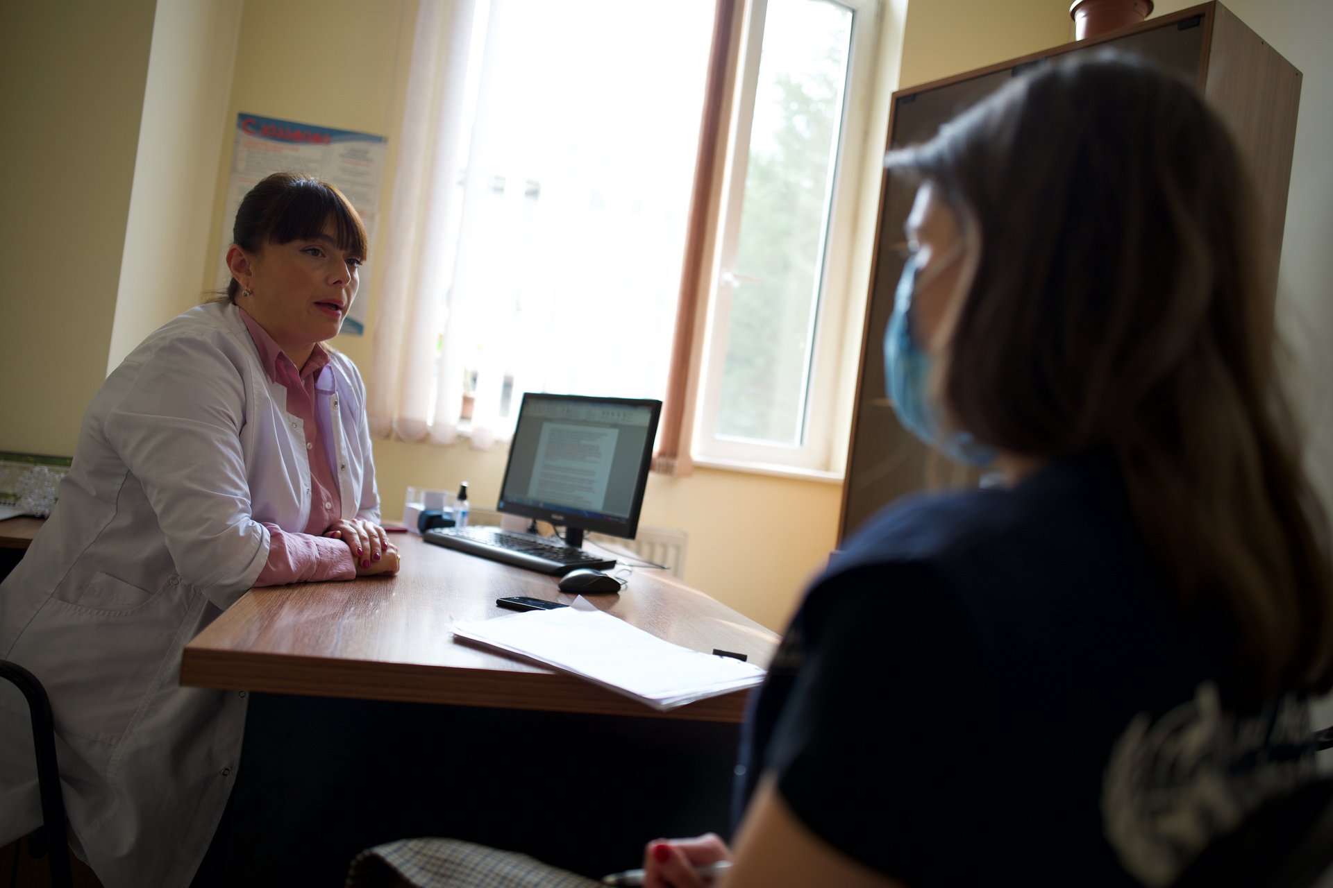A health-care provider speaks with a patient in an office.