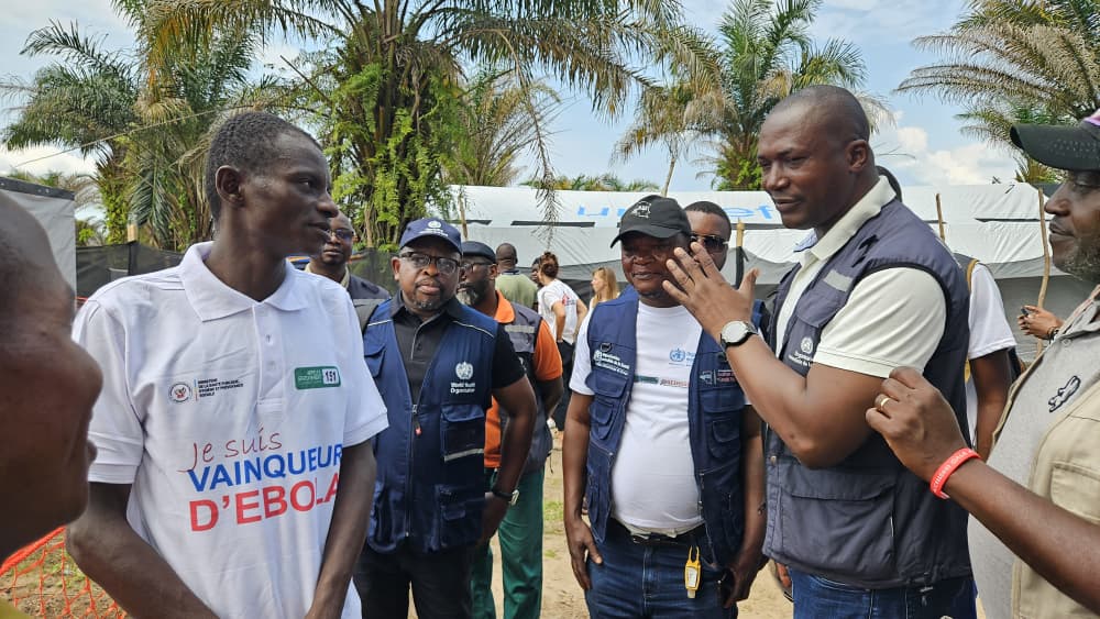Ebola patient leaving treatment centre Men wearing WHO vests with a man with an Ebola survivor T-shirt