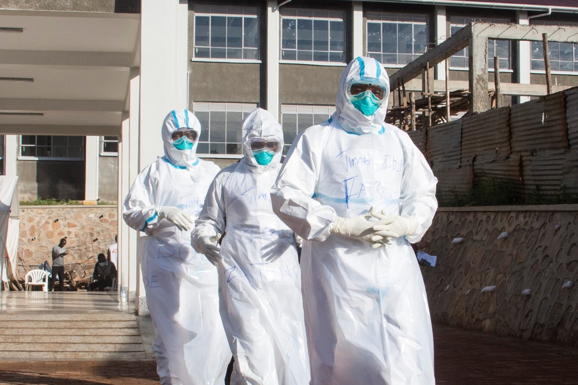 Three health-care workers wearing personal protective equipment (PPE) are walking in a row.