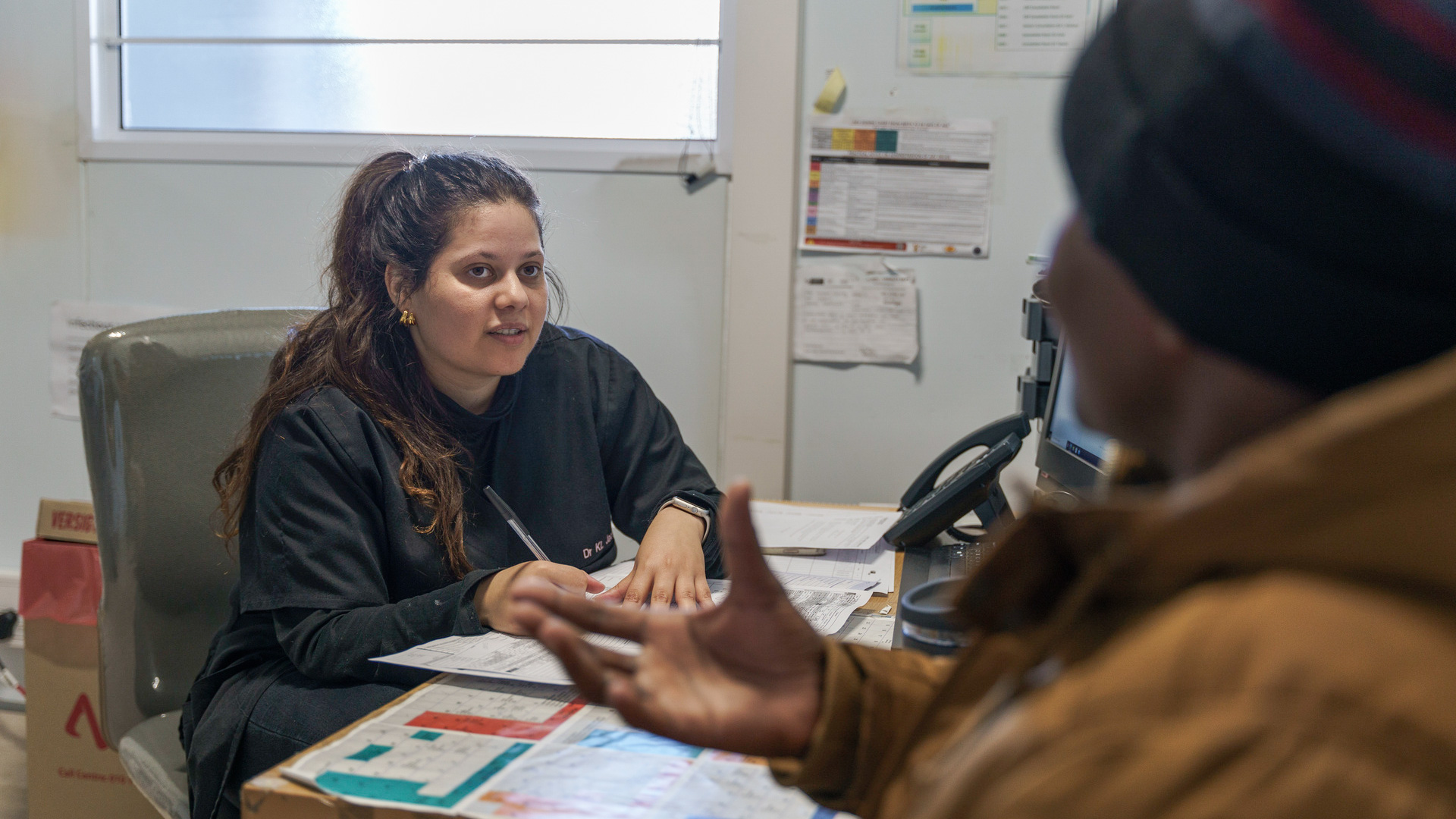 A female doctor is attentively listening to a patient who is gesticulating with his hand.