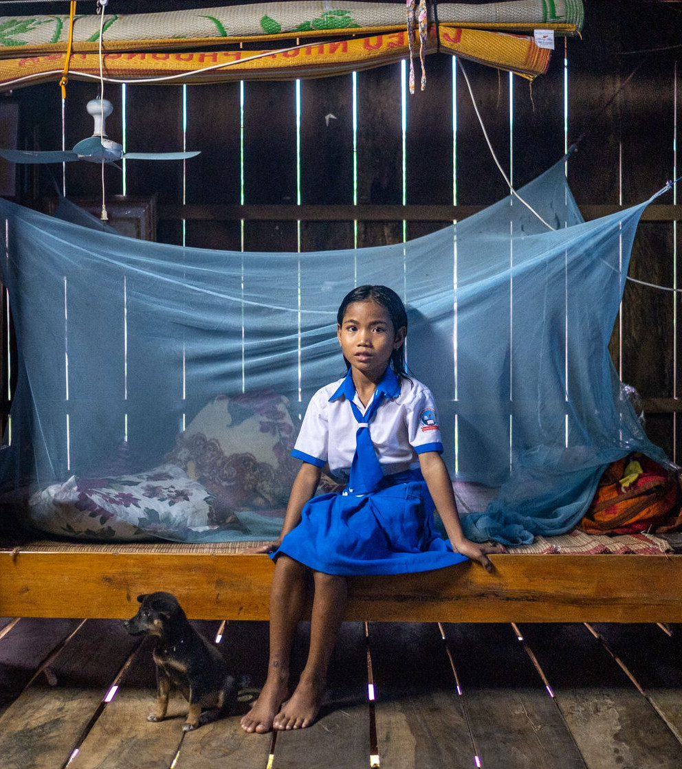 Girl sitting at a bedside a bednet in the background