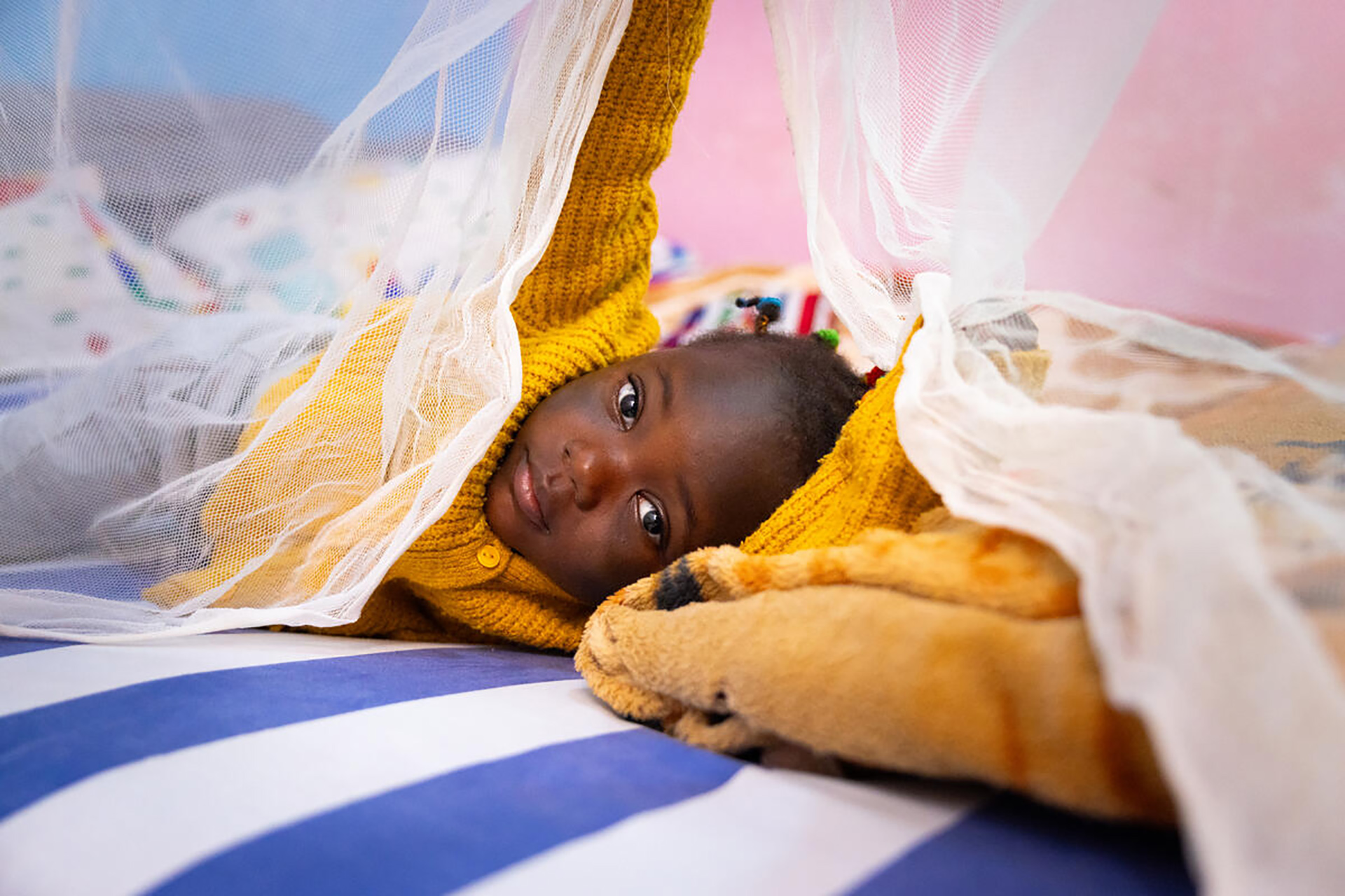 Child lying on bed with mosquito net in Cameroon Young girl sleeping under a dual-insecticide net in Cameroon