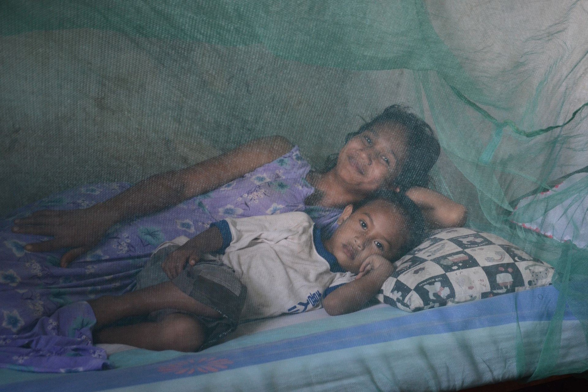 Children under mosquito bed net in Timor-Leste Two children lay in a bed under a mosquito net.