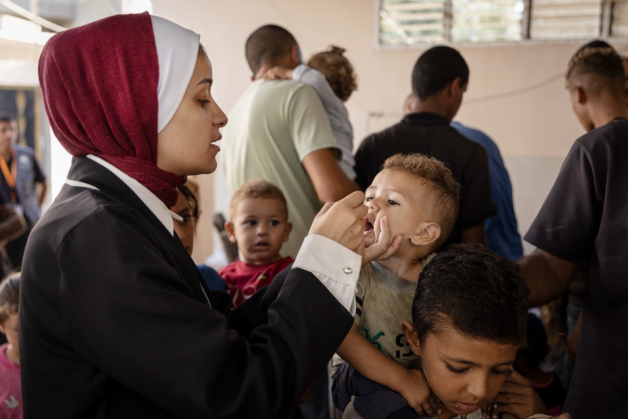 Oral polio vaccine given to young child A female vaccinator gives oral polio vaccine to a young child who is sitting on his brothers' shoulders .