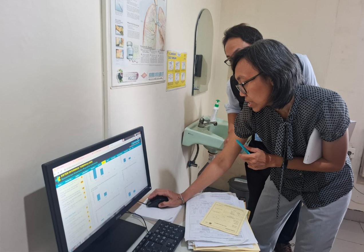 A team of tuberculosis epidemiological review team in Setiabudi community health centre in Jakarta. A woman is looking at a computer monitor while standing, accompanied by a man beside her.