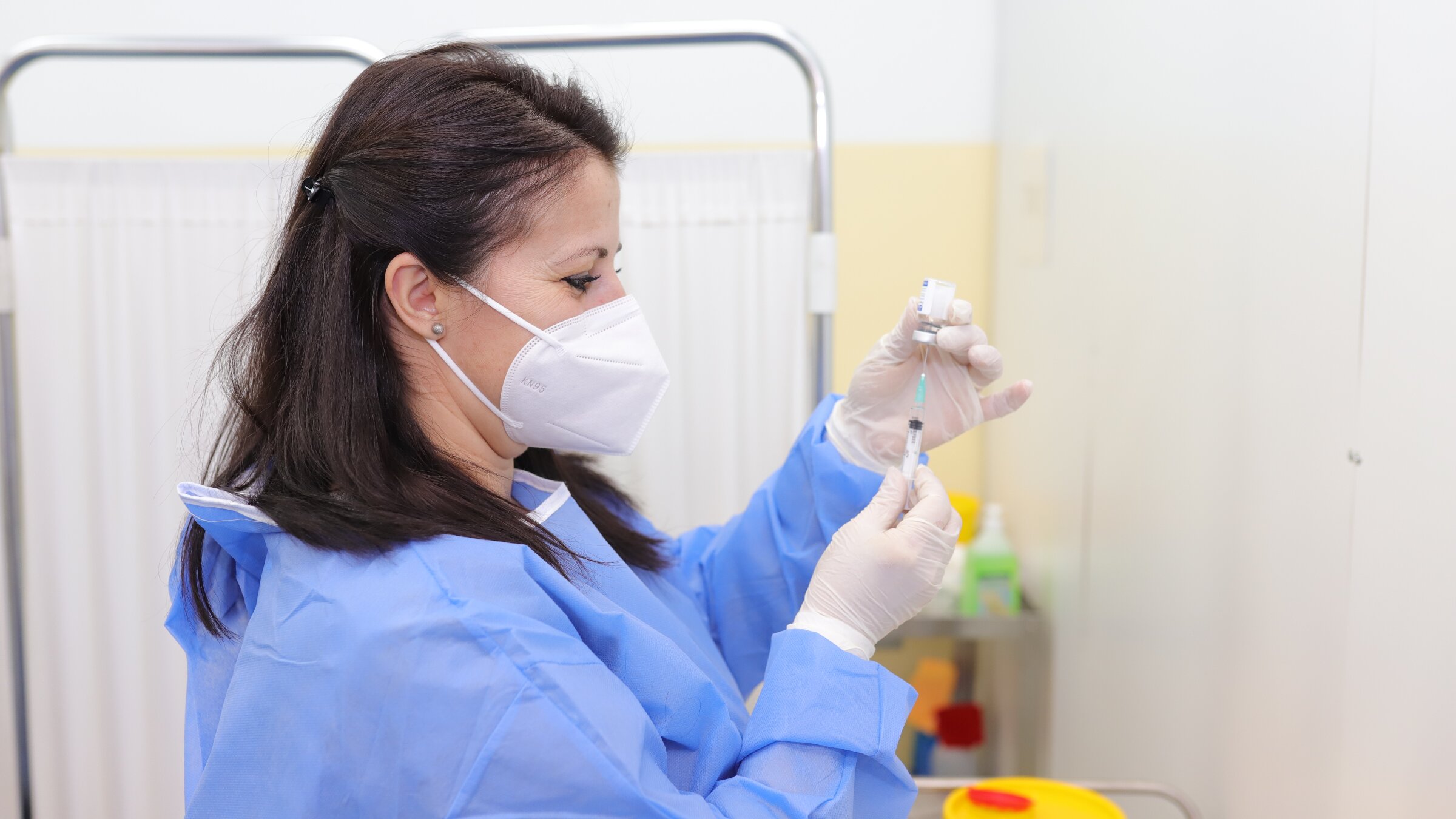 Routine Immunization A female doctor or nurse in protective clothing extracts vaccine into syringe.