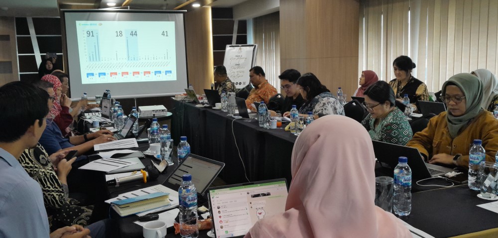 A meeting room with participants discussing and looking at the projector screen.
