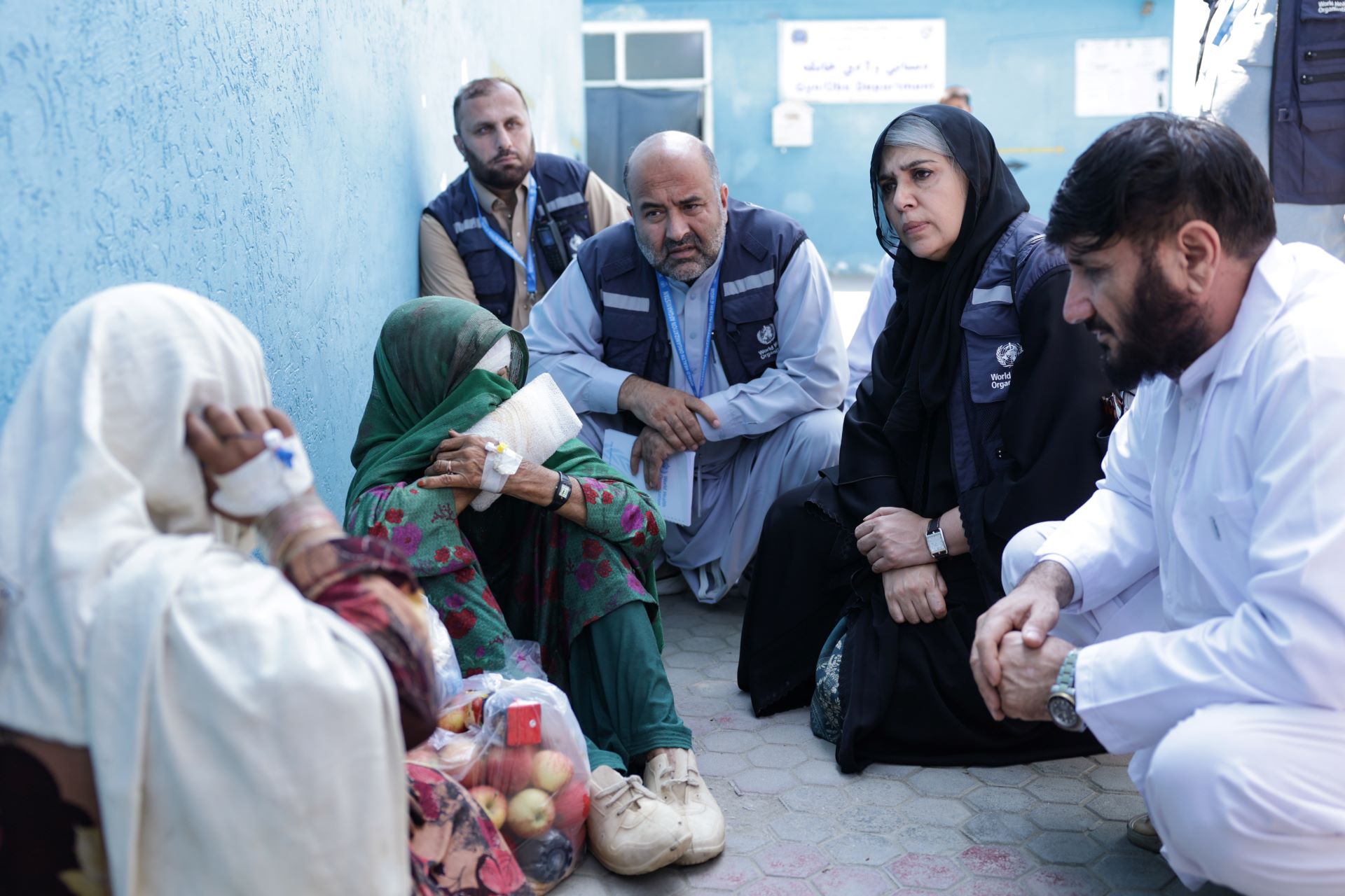 Kunar earthquake 2025 Several people in WHO vests crouching beside two wounded women.