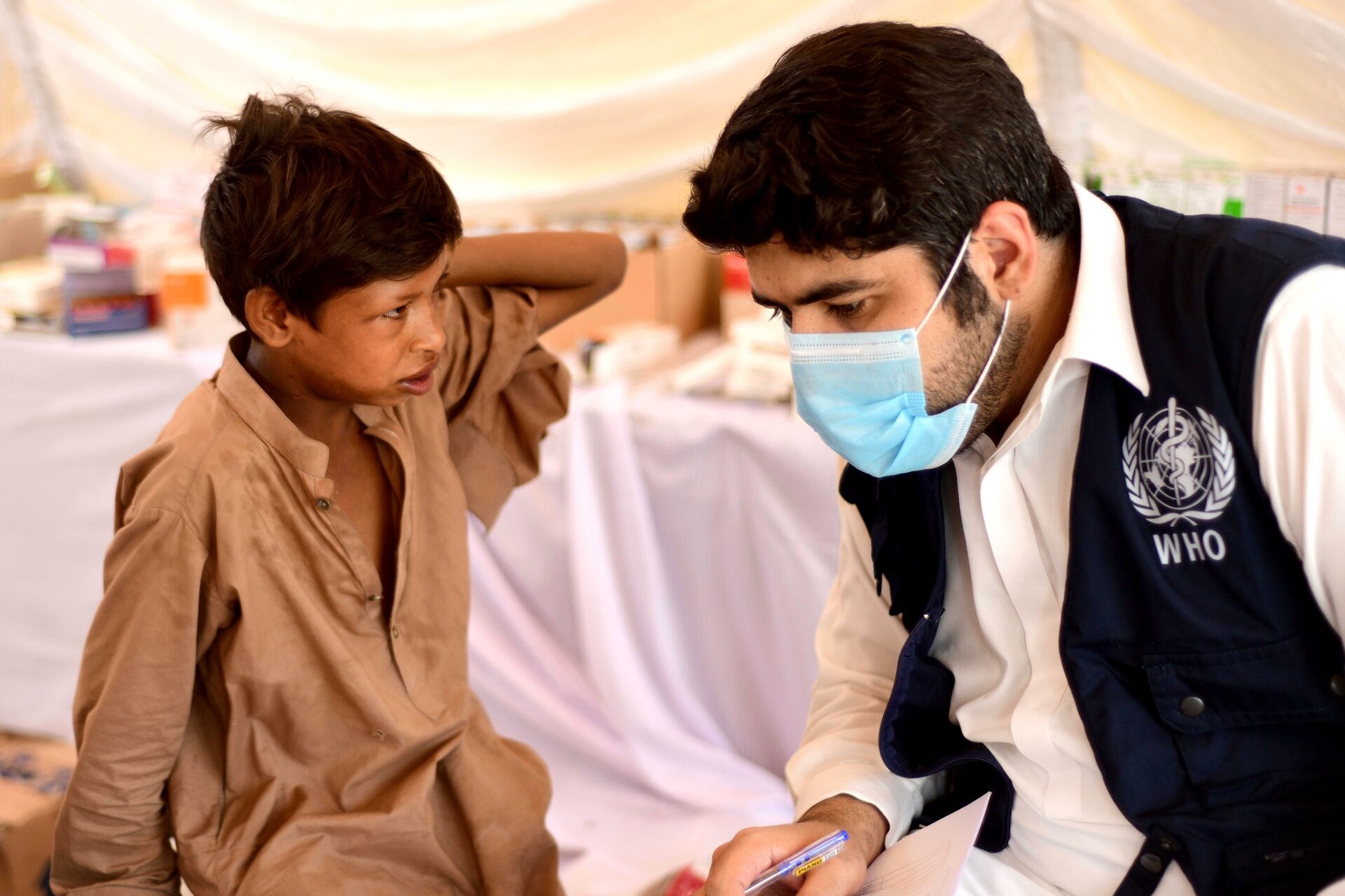 Man in surgical mask and WHO jacket sits with young boy.
