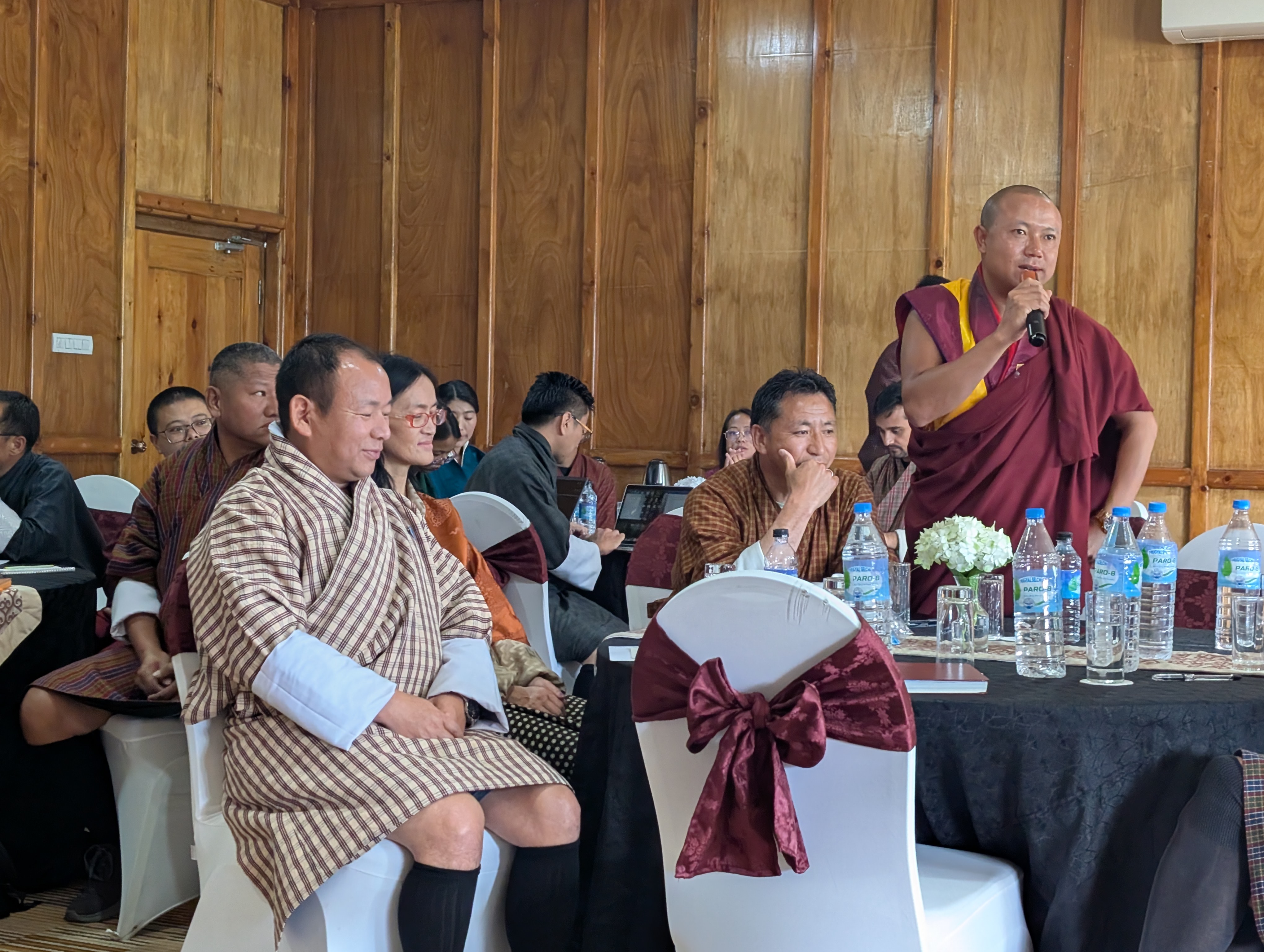A group of people sitting around a table and one man standing up talking on a mic