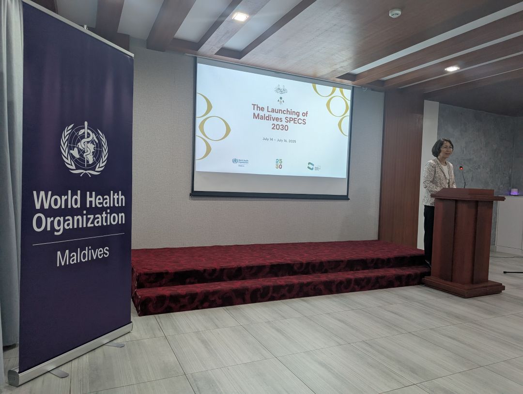 A woman talking on a stage . WHO Maldives banner on the left side