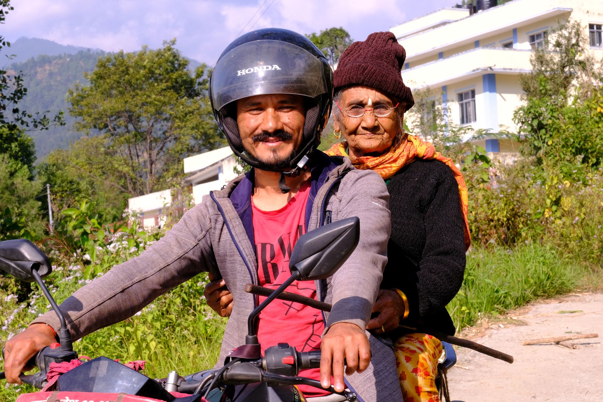 A woman and a man on a motorbike. The woman is wearing eyeglasses