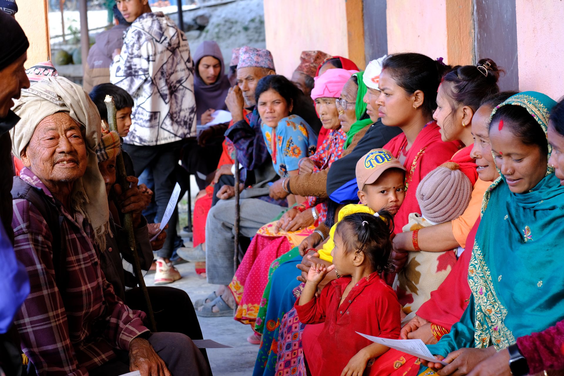 A group pf women, men and children waring colourful clothes and all sitting down