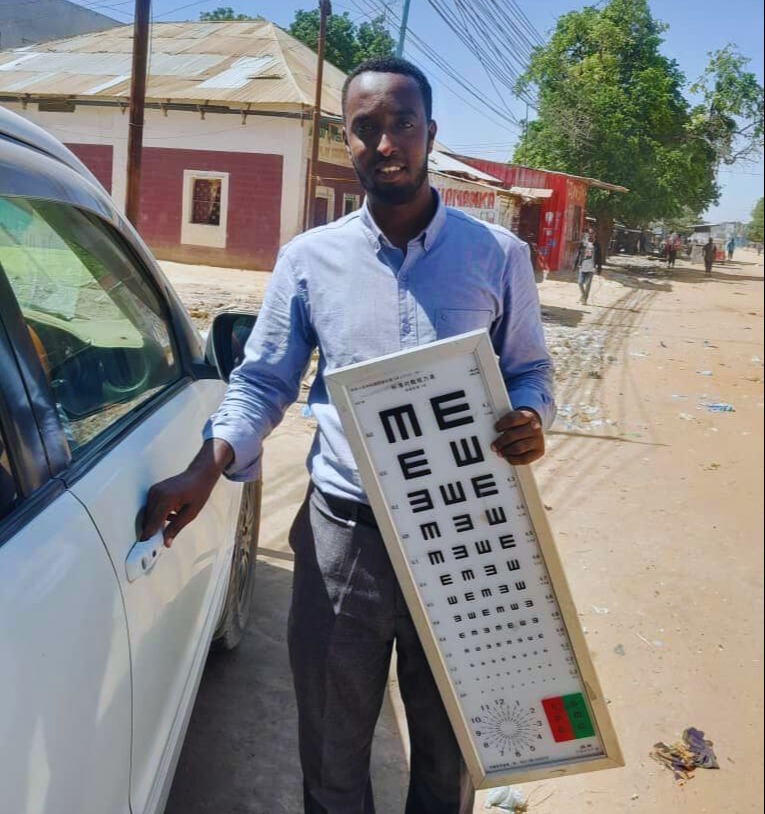 A man holding an eye chart and opening a car door