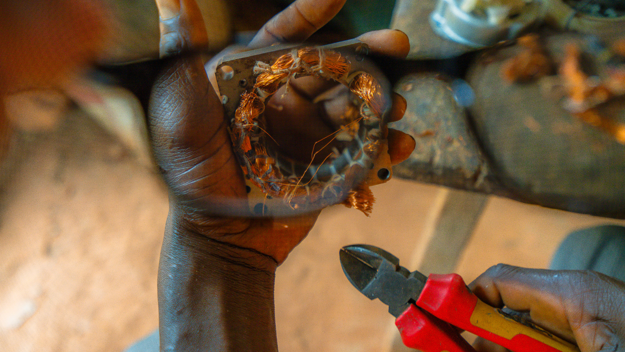 RestoringVision 1 A close-up view of a person’s hands repairing an electrical component, seen through a pair of eyeglasses.