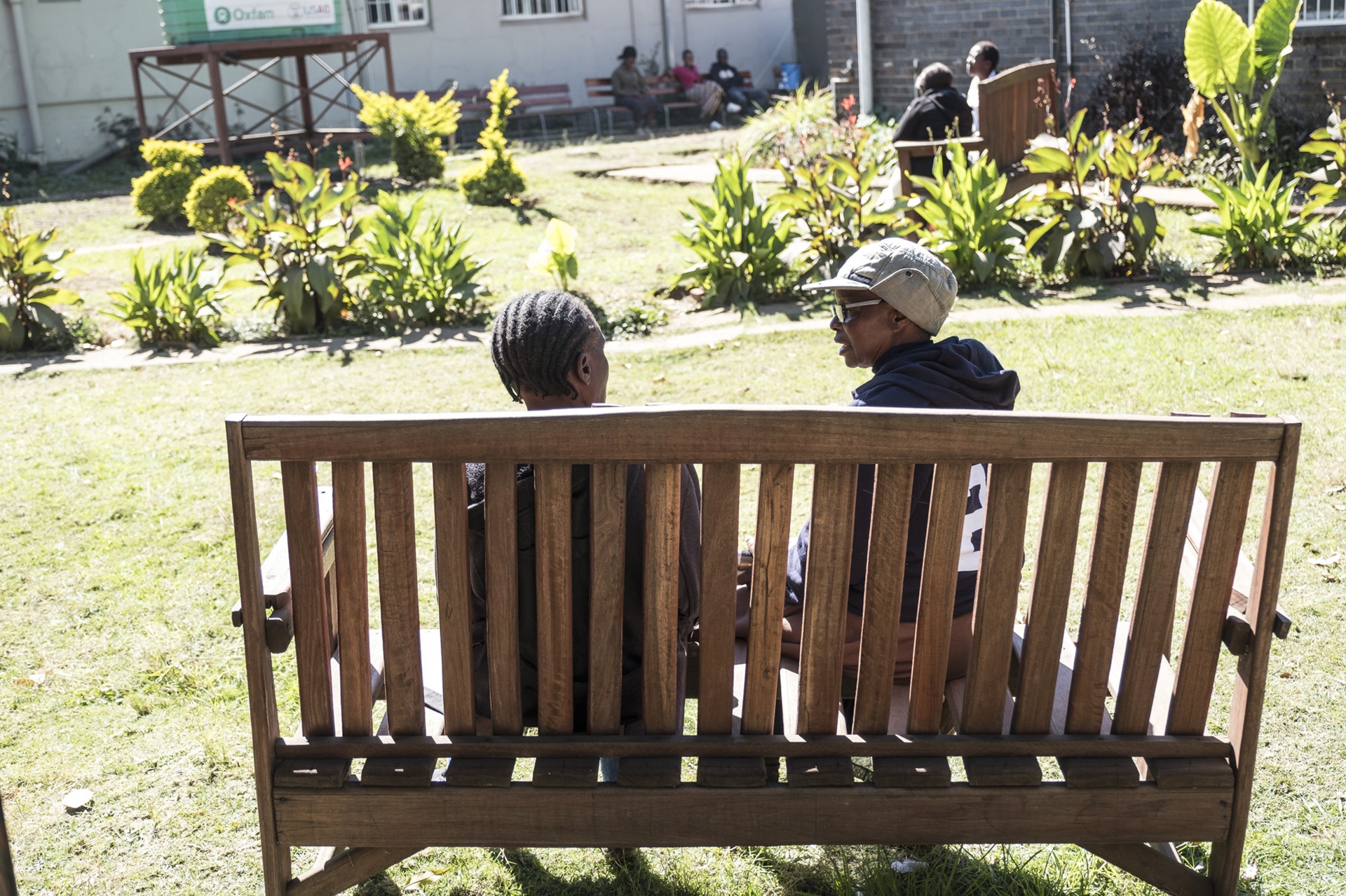 Two people sit on a wooden bench in a park setting