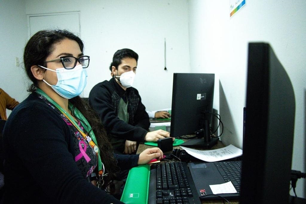 Two people in an office, wearing face masks working on computers.