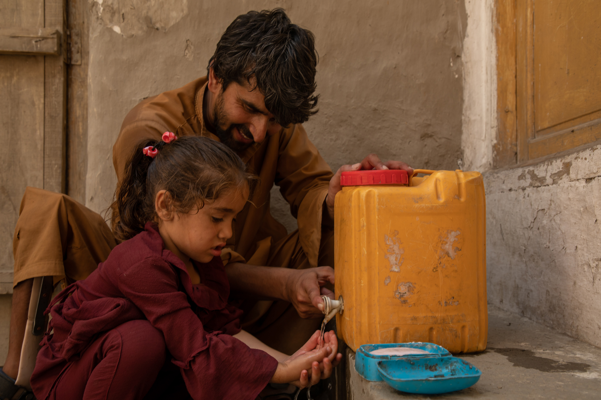 hand hygiene 101525-2000px a young man helps a little girl to wash her hands at a small hand washing station in a village in Afghanistan