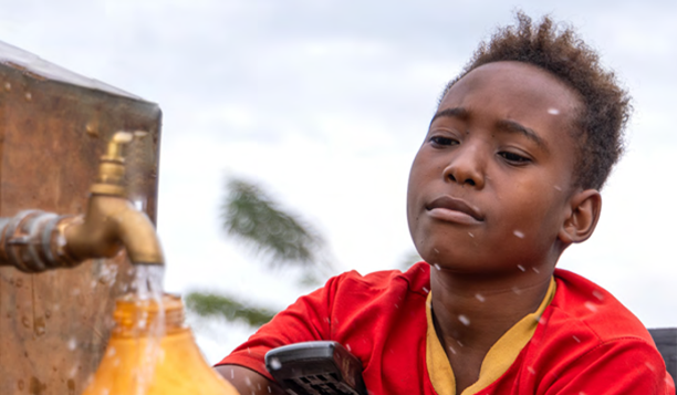 JMP25-cover-612X357px an African boy dressed in a red teeshirt collects water from a tap