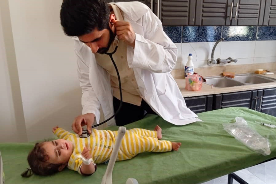 A doctor examines a baby who is lying on an examination table, listening through a stethoscope.