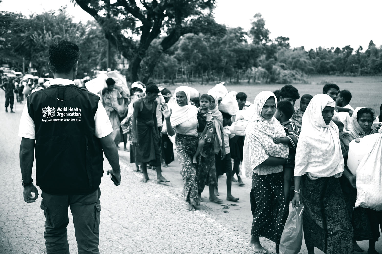 Refugees on the march Refugees are walking on the side of a road, a WHO officer is observing the event.