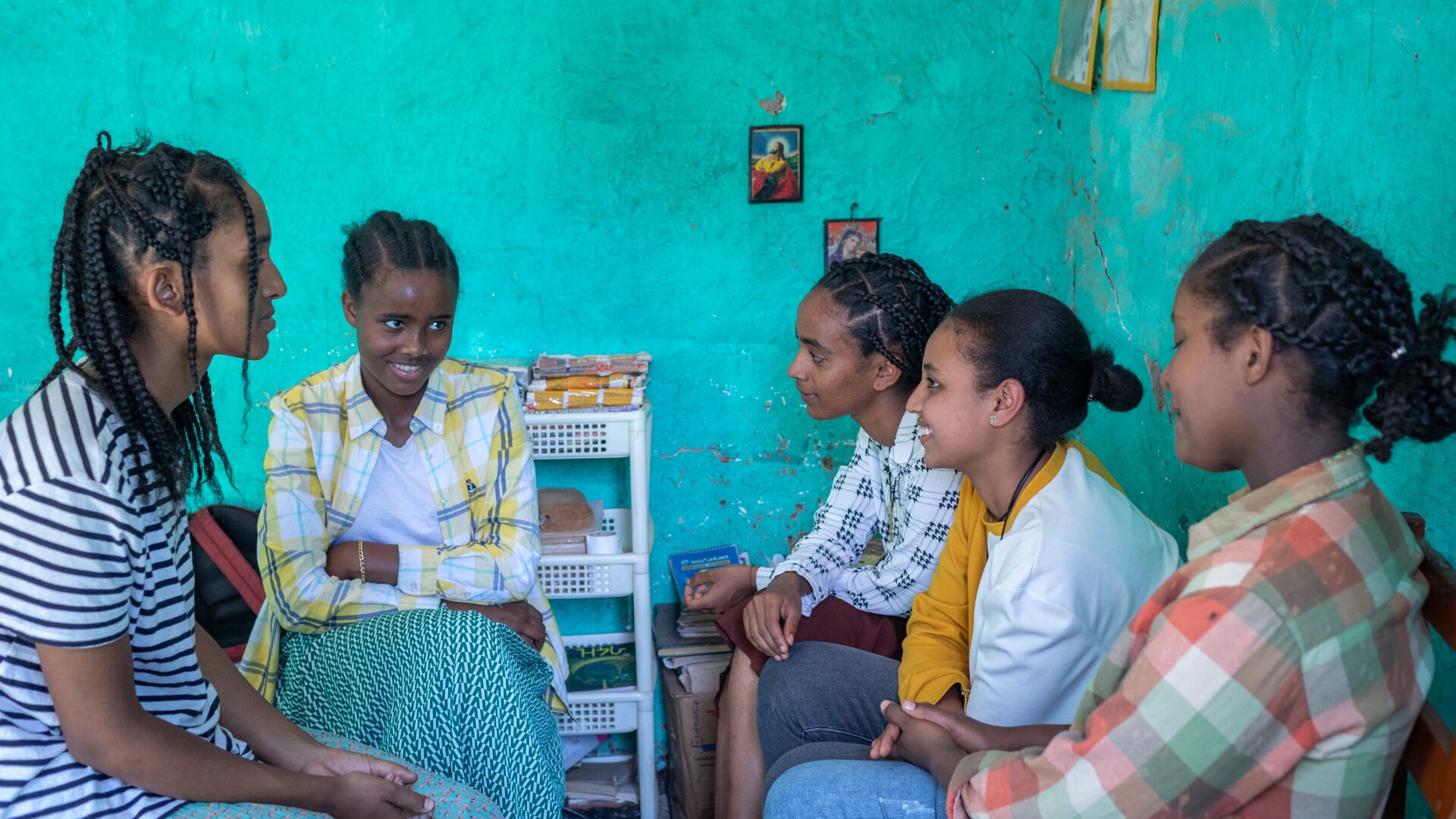 Five adolescent girls sitting in a room talking to each other.