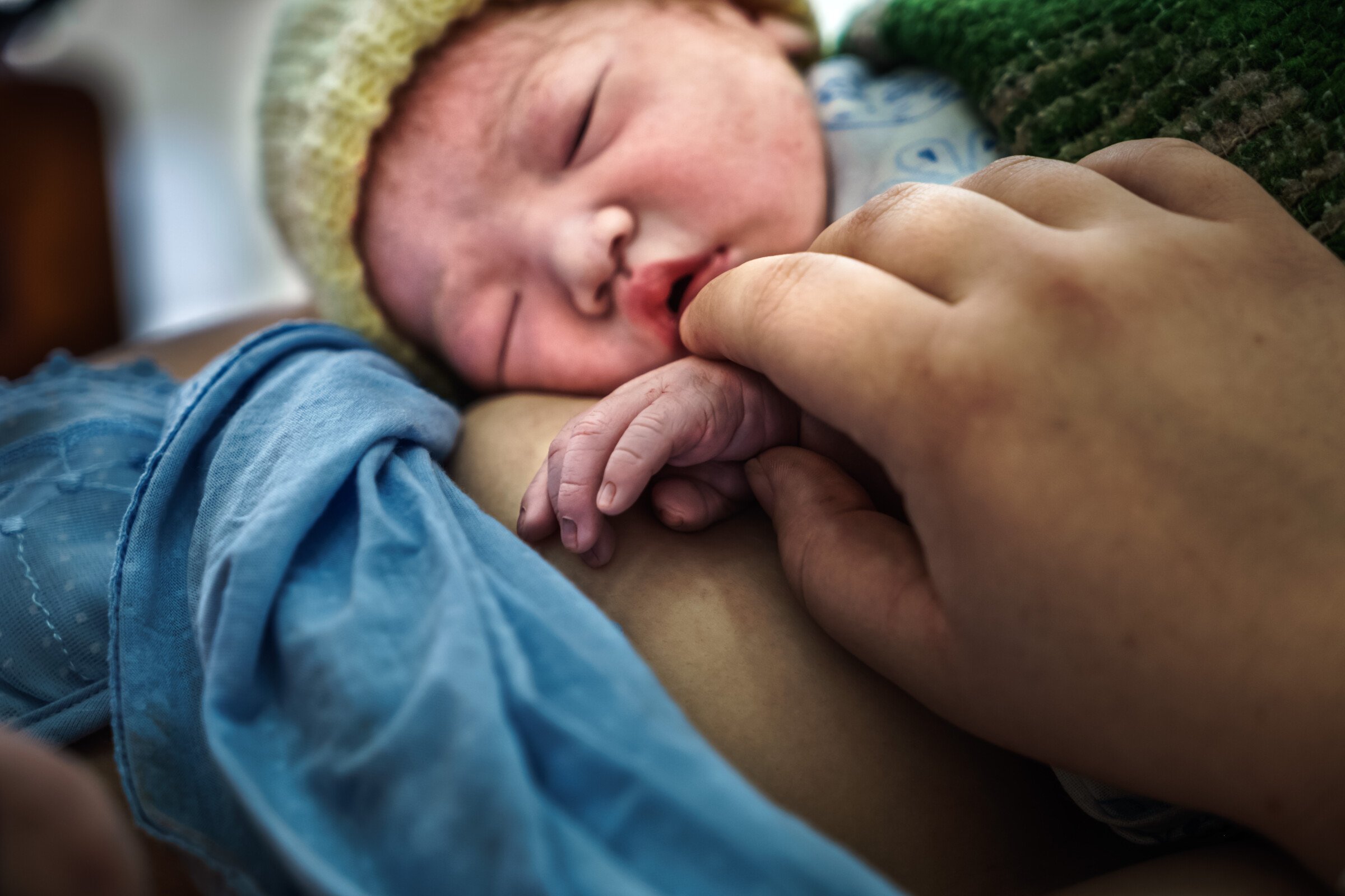 A newborn baby is laying on his mother's breast as she holds its hand.