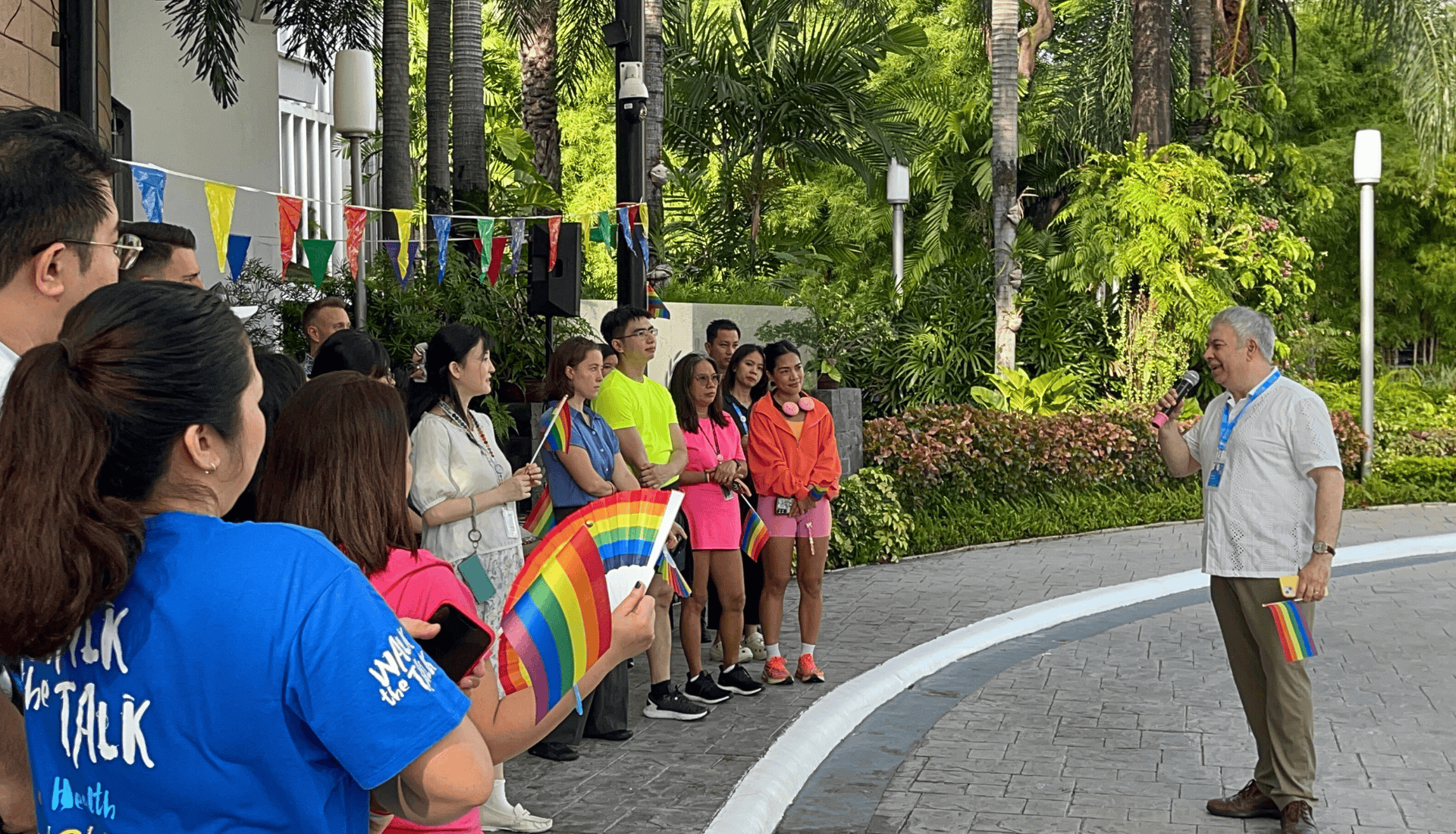 A man speaks in front of people holding Pride flags