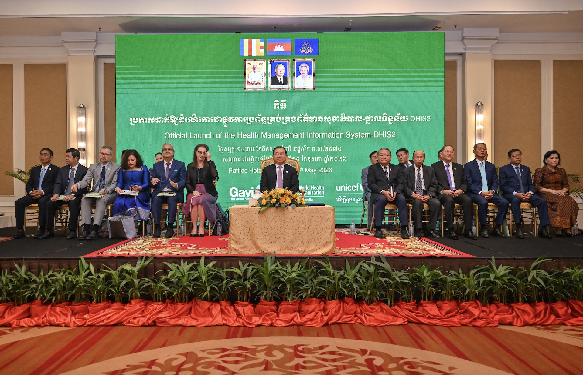 Officials seated on stage at Cambodia’s DHIS2 health information system launch with green backdrop and partner logos.