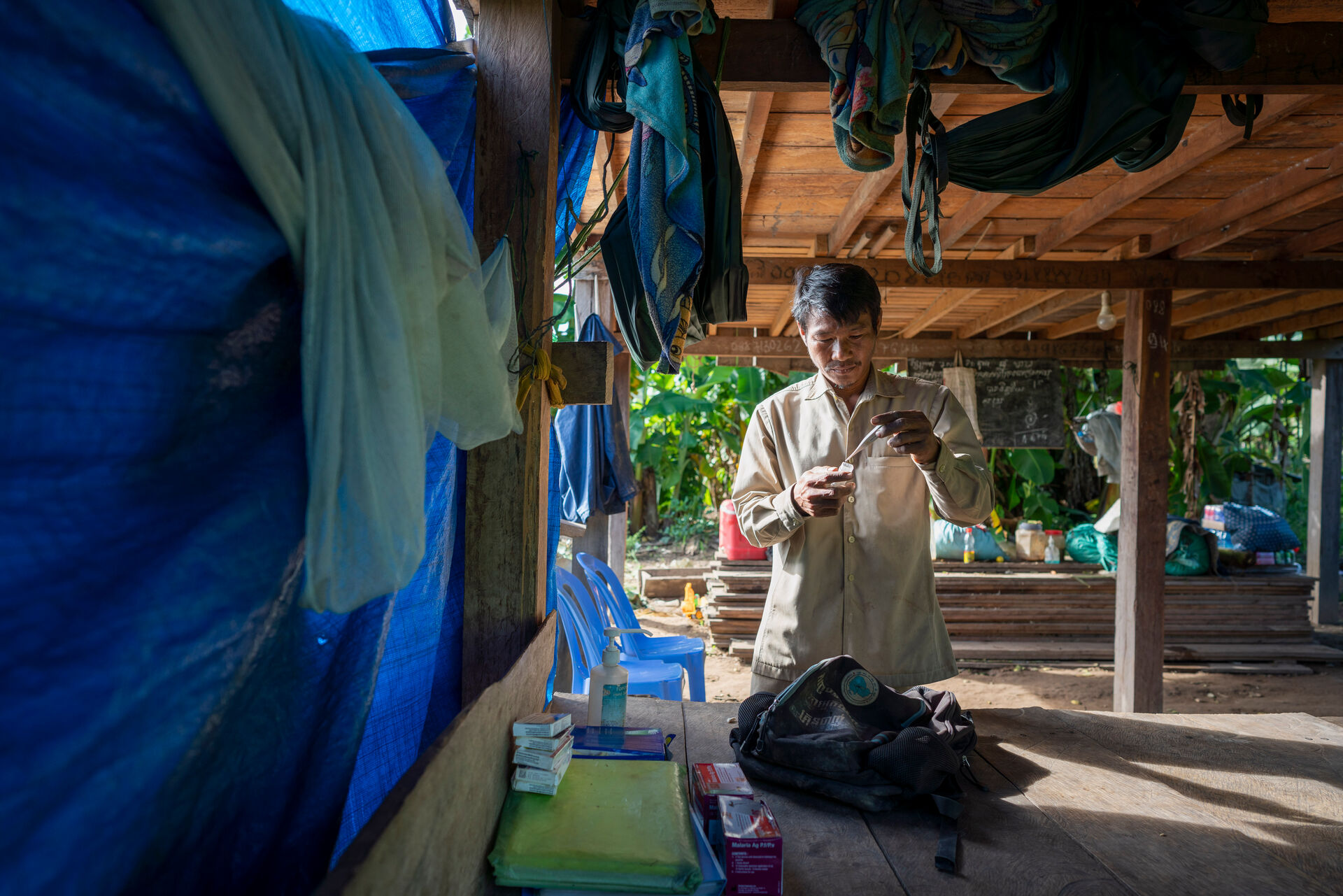 Health worker prepares malaria test supplies in a rural shelter, with diagnostic kits on a wooden table.