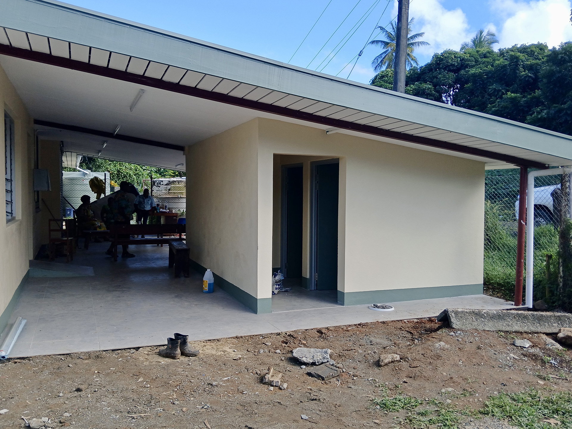 Newly renovated building with covered open area and two doorways, surrounded by trees and utility poles.