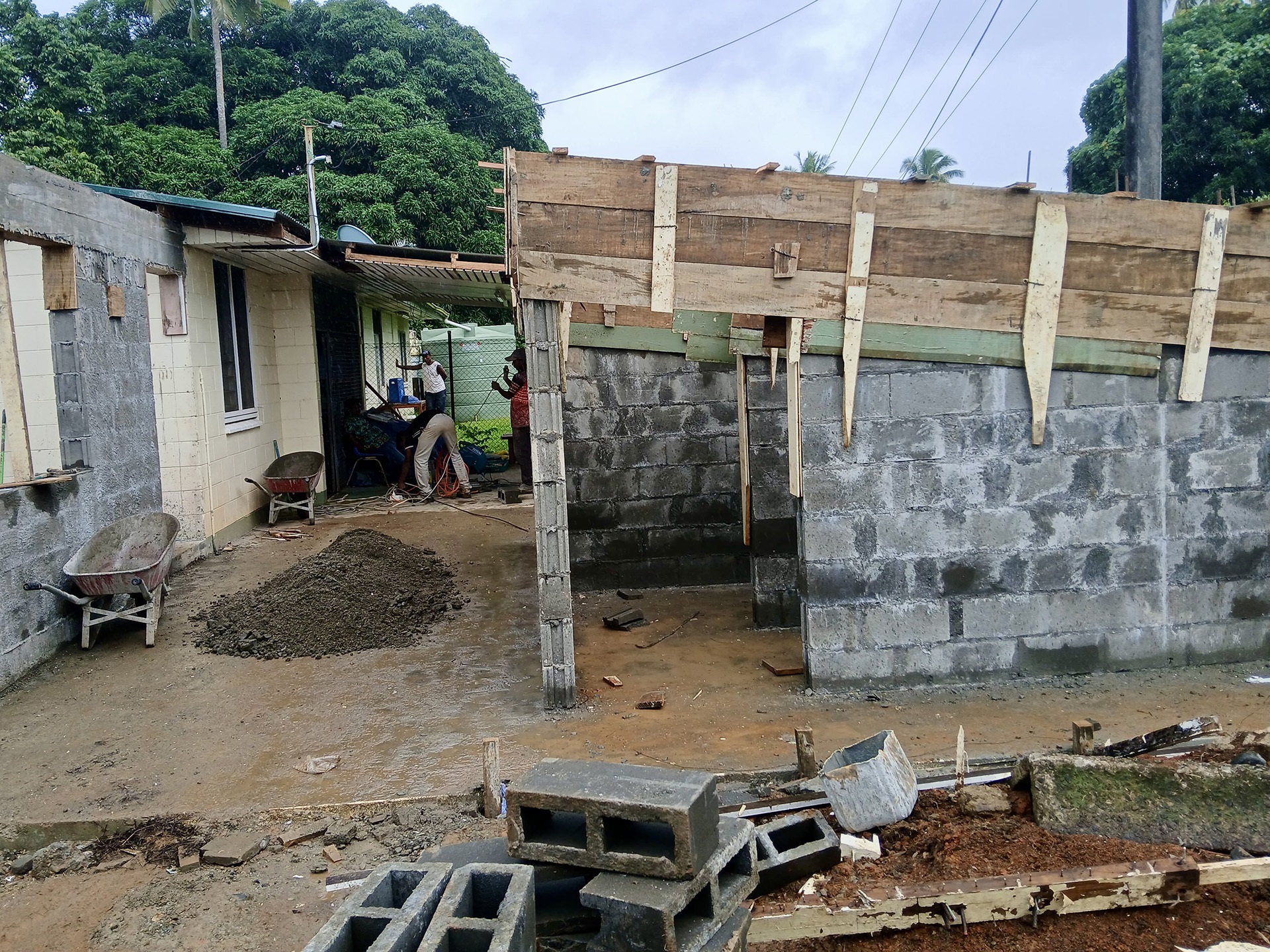Coconut halves drying on a corrugated roof near thatched huts, palm trees, and hanging laundry in a tropical village.