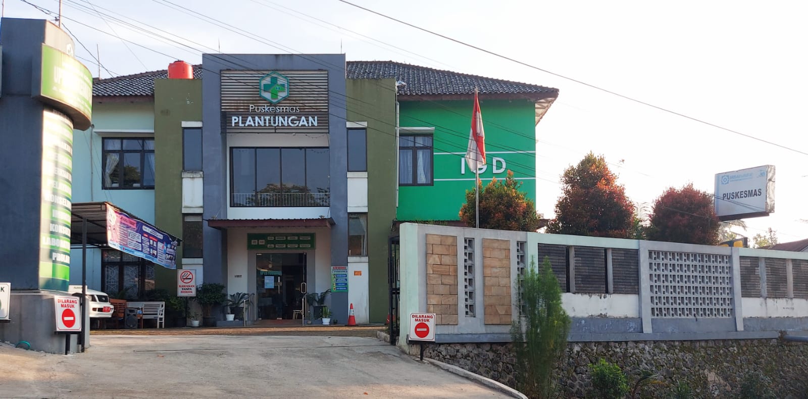 Pintu masuk depan Puskesmas Plantungan, fasilitas kesehatan berwarna hijau dan putih dengan namanya pada papan, bendera Indonesia