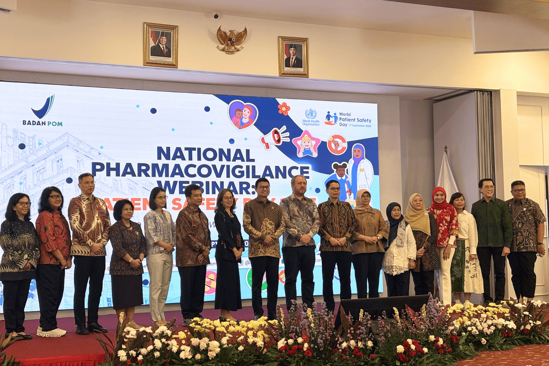A group of people poses for a photo onstage. Behind them is text that says national pharmacovigilance webinar