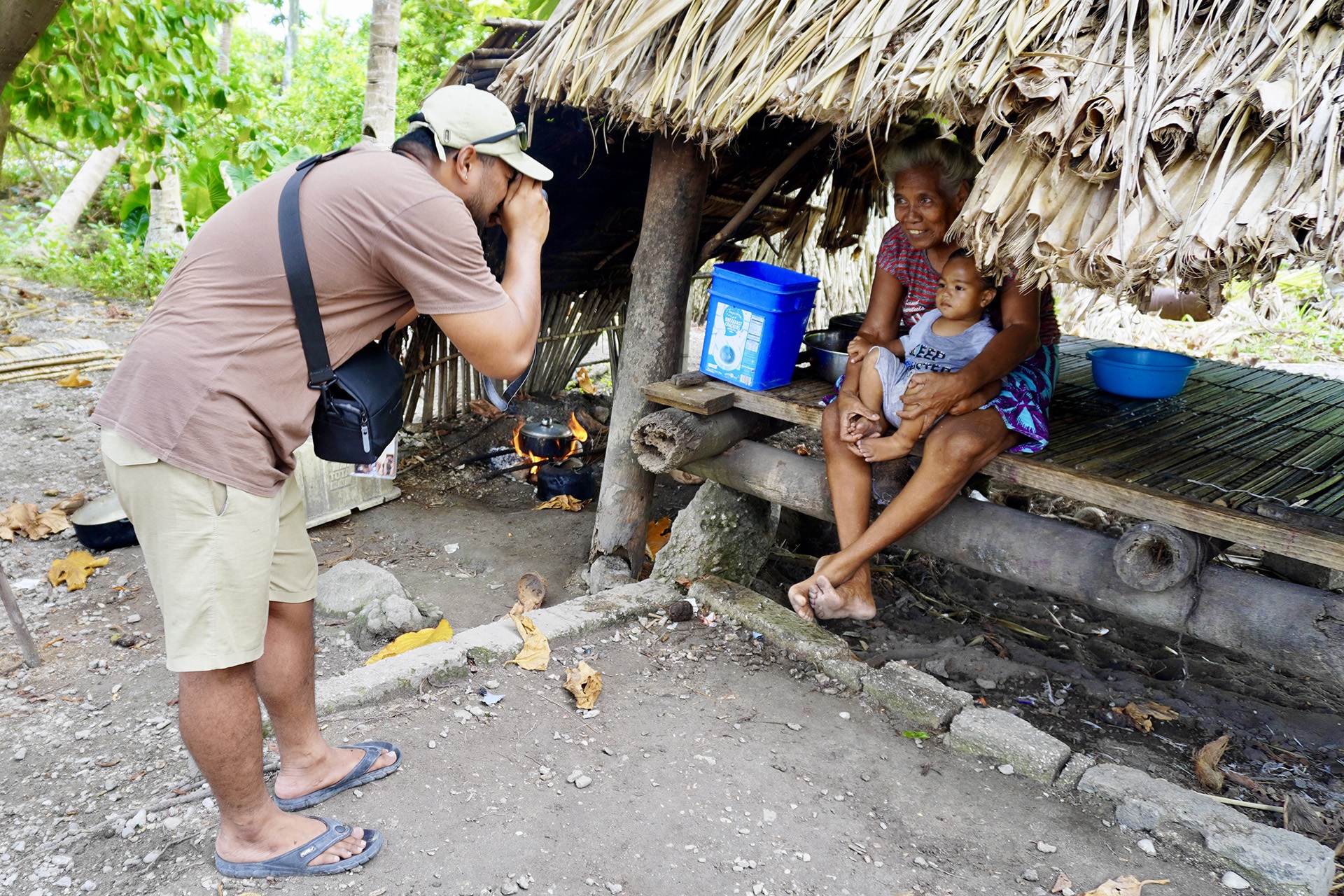 Person taking a photo of two people sitting under a thatched hut.