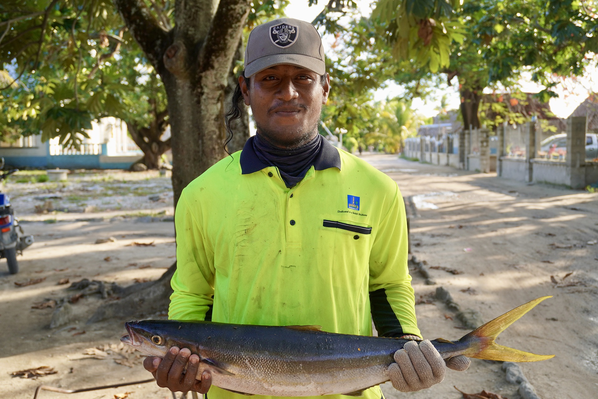 Coconut halves drying on a corrugated roof near thatched huts, palm trees, and hanging laundry in a tropical village.