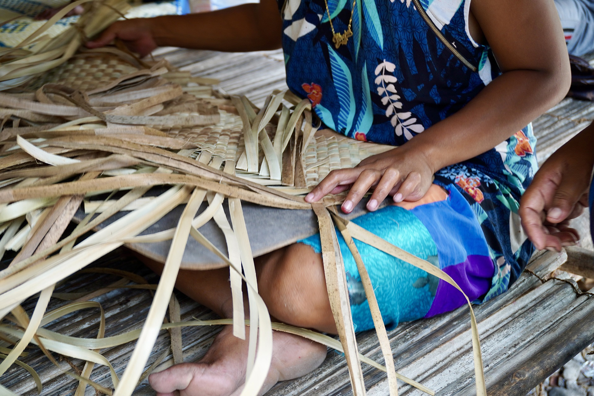 Coconut halves drying on a corrugated roof near thatched huts, palm trees, and hanging laundry in a tropical village.